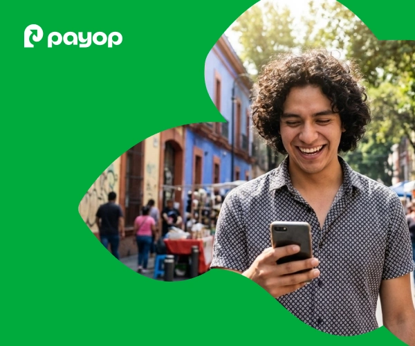 A smiling person with curly hair looks at their phone on a vibrant street with colourful buildings and trees. PayOp logo on green overlay in the corner.