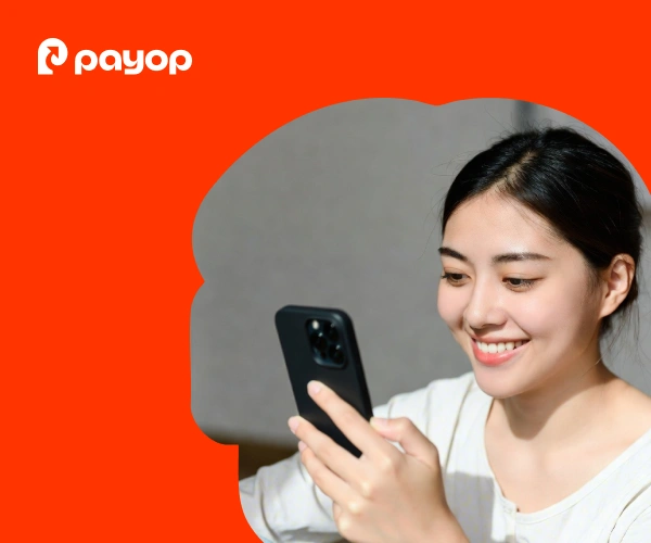  A woman smiles as she looks at her smartphone against an orange background with a wavy border. The Payop logo is in the top left corner.
