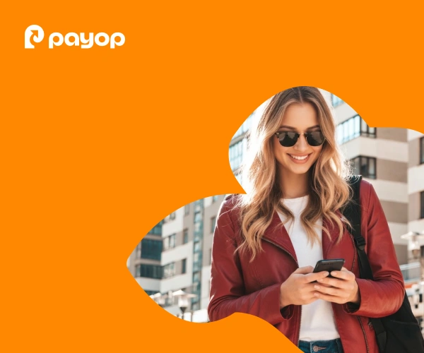 Smiling woman in sunglasses and red jacket using her phone, set against an abstract orange design with Payop logo, urban buildings in the background.