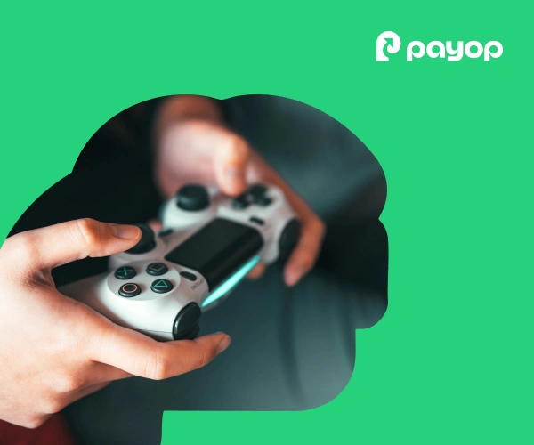 Hands holding a video game controller against a bright green background with the Payop logo. The scene conveys focus and engagement.