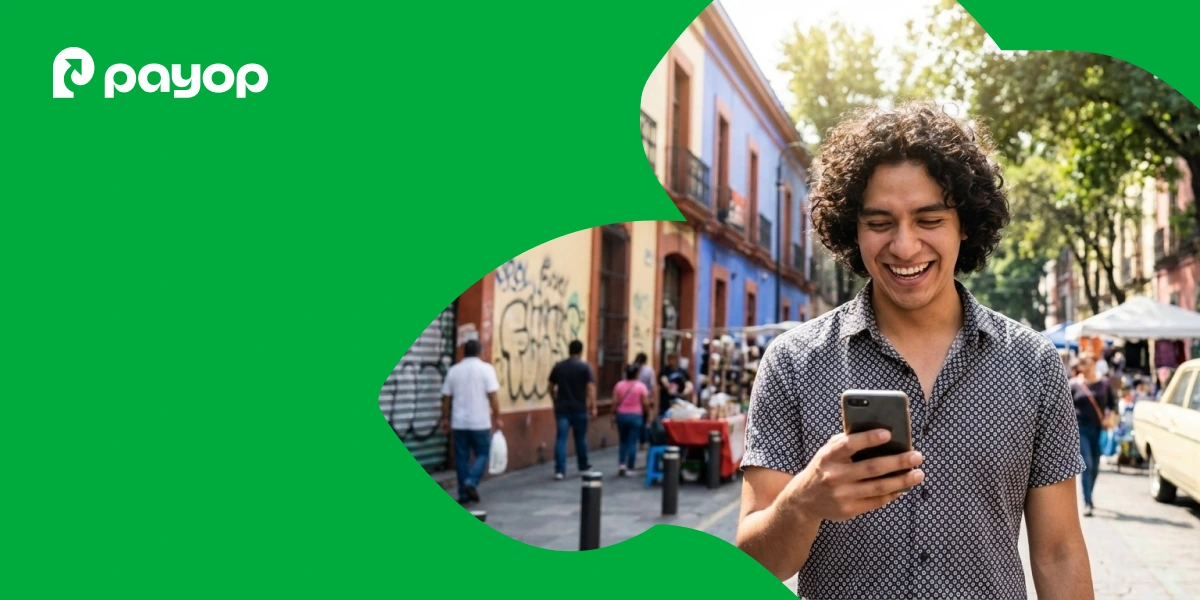 A smiling person with curly hair looks at their phone on a vibrant street with colourful buildings and trees. PayOp logo on green overlay in the corner.